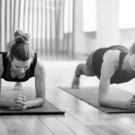 Front view of two sporty fit and slim middle aged women doing planking exercise indoors together with a natural light in modern interior sport studio hall or yoga class.