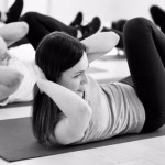 Attractive woman and group of young sporty people practicing in sport gym, doing crisscross pose, bicycle crunches exercise, working out, indoor full length, students training in fitness club, studio